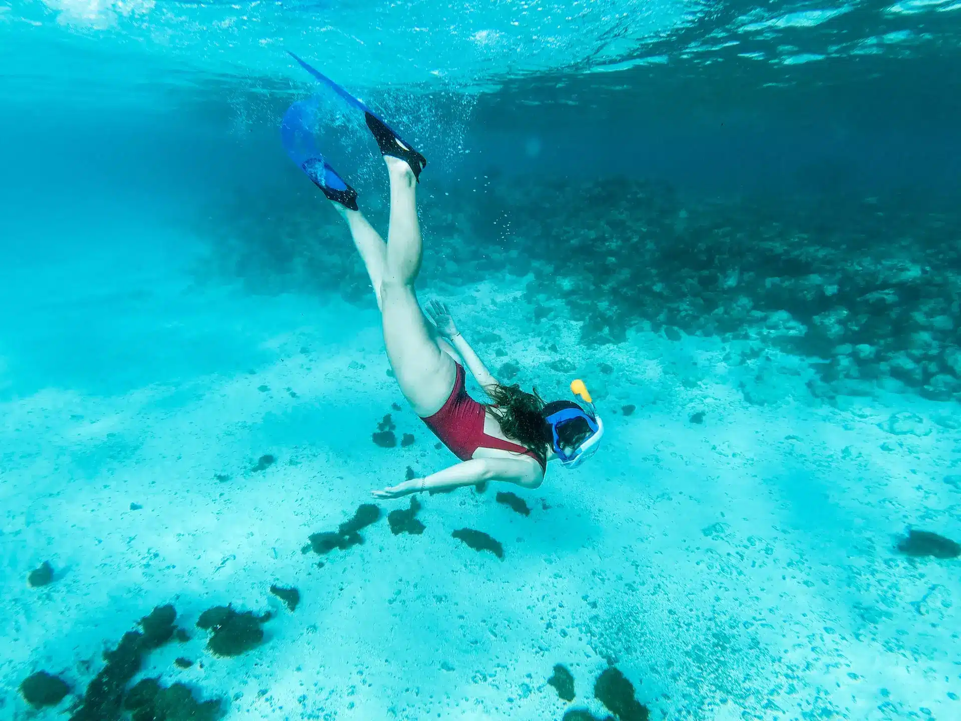 Ragazza che fa snorkeling in apnea su un fondale sabbioso con coralli
